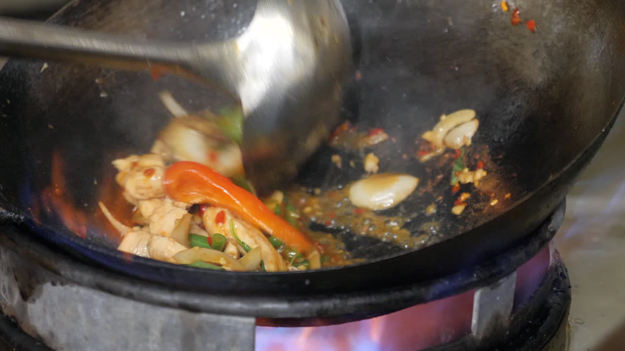 Nærbillede af en kok, der woksteger kylling med chili og basilikum, kendt som en populær ret i Thailand.