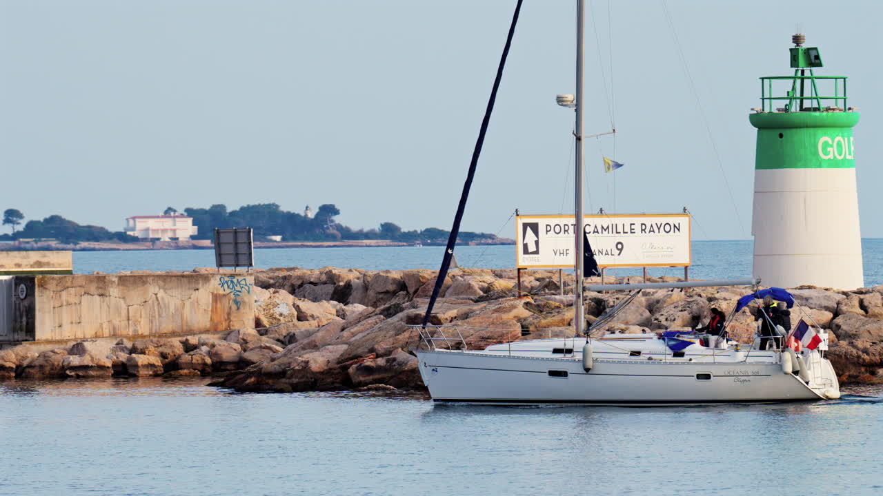 Antibes, France - February 14, 2025: Boat with the flag of France moving on the sea on a cloudy day near a lighthouse
