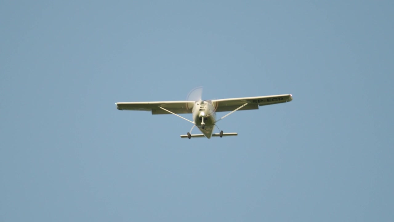 Piccolo aereo a elica che vola contro un cielo azzurro limpido. L'aereo si avvicina alla telecamera durante un volo diurno, mostrando il suo carrello d'atterraggio.