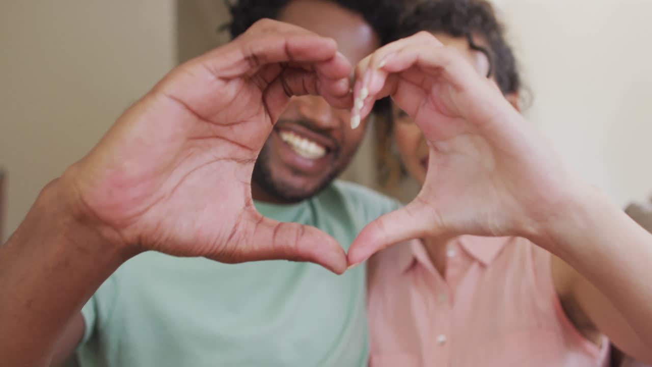 feliz pareja biracial haciendo gestos de corazón con las manos