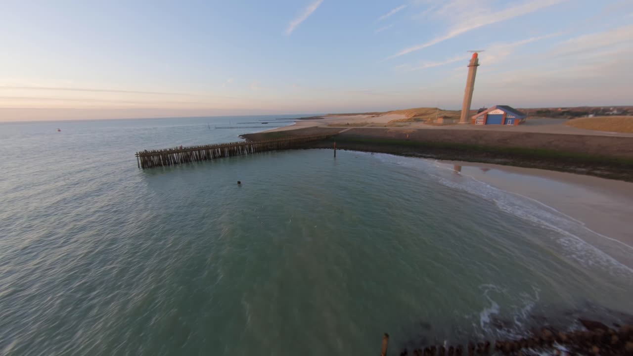 drone volando rápido desde el mar hacia un dique con un muelle y un faro