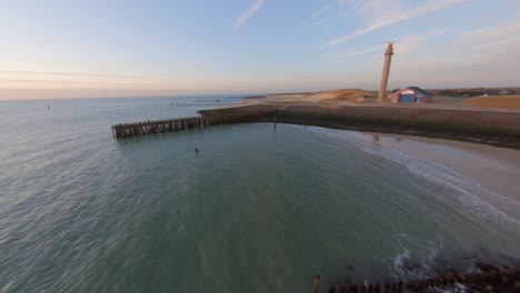 drone flying fast from the sea towards a dyke with a pier and lighthouse