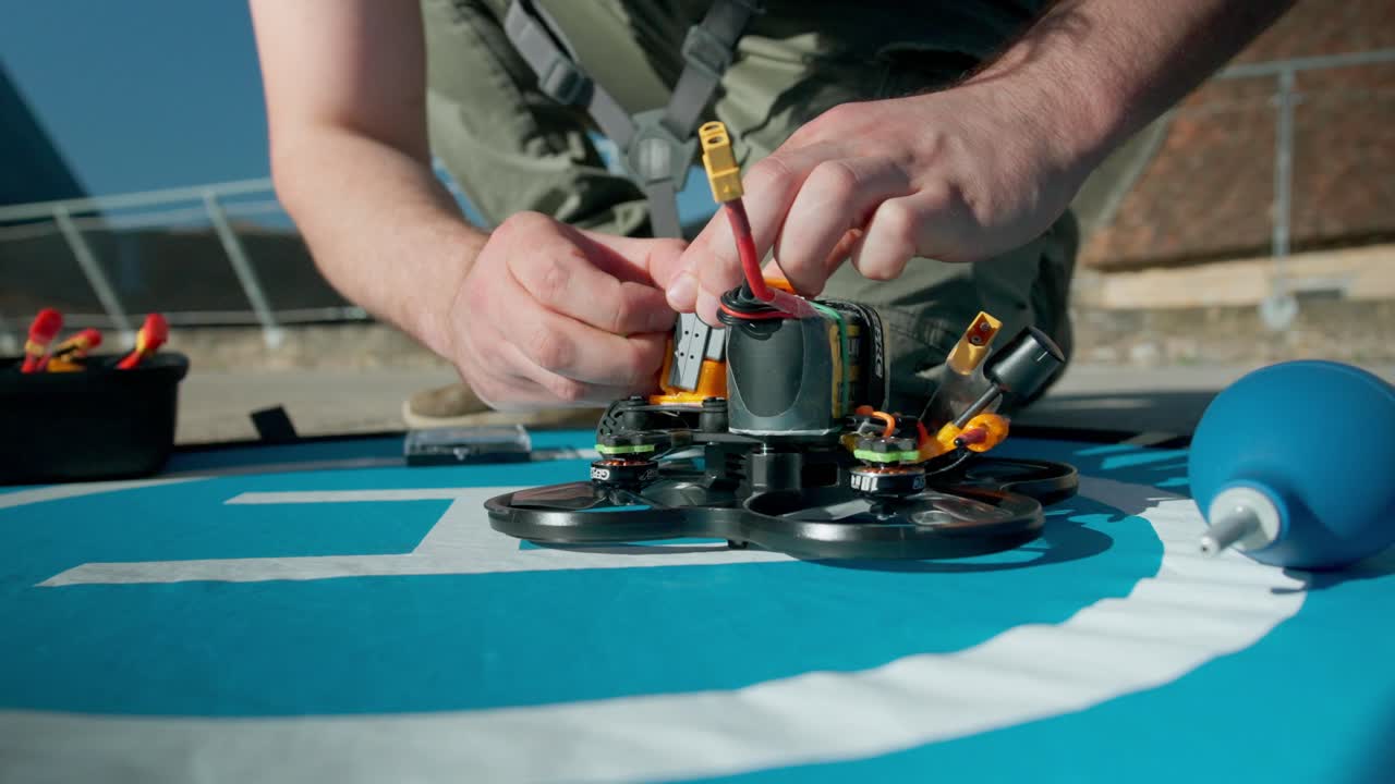 Person adjusting the wiring and securing the battery on a small quadcopter sitting on a blue mat with tools nearby