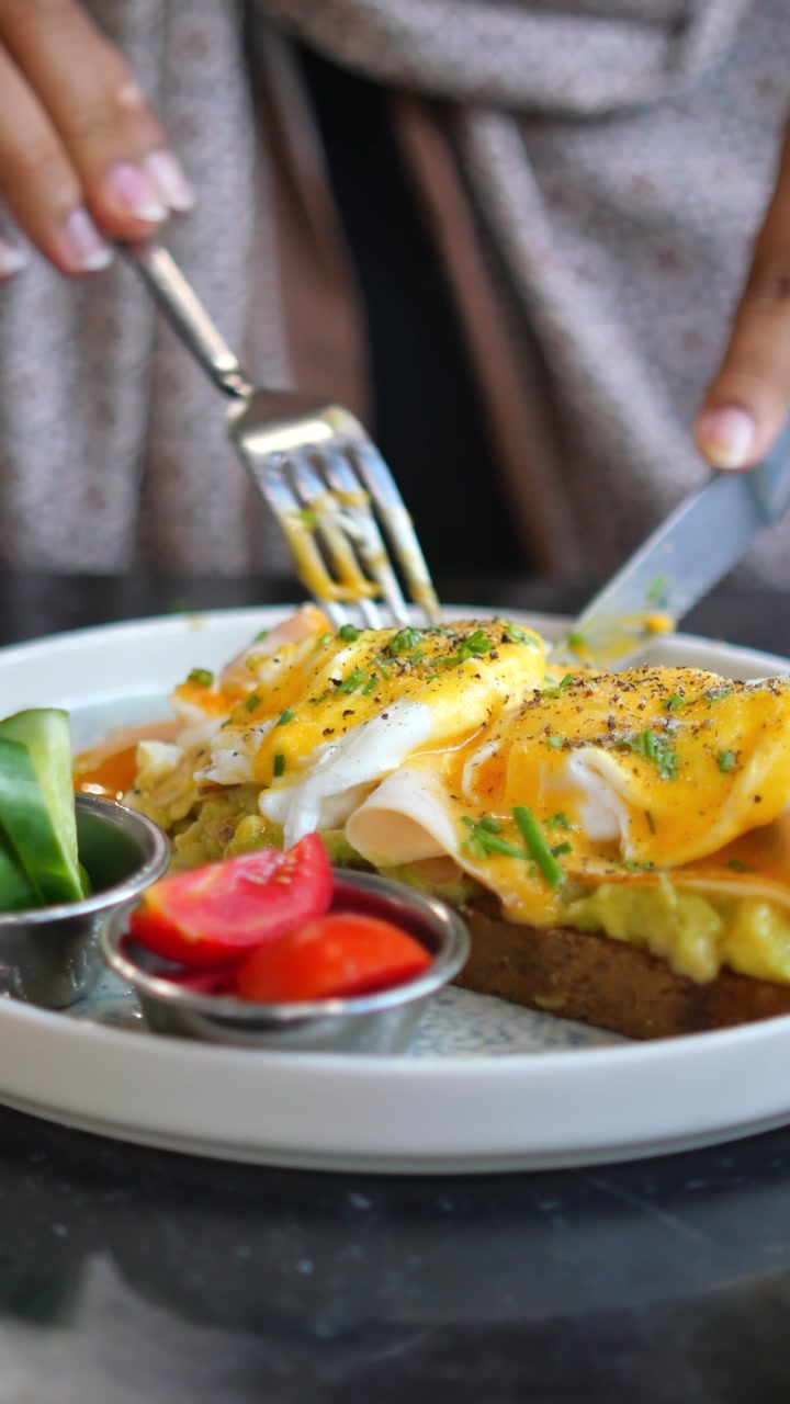 Close-up of a Person Cutting and Eating Avocado Toast with Poached Eggs