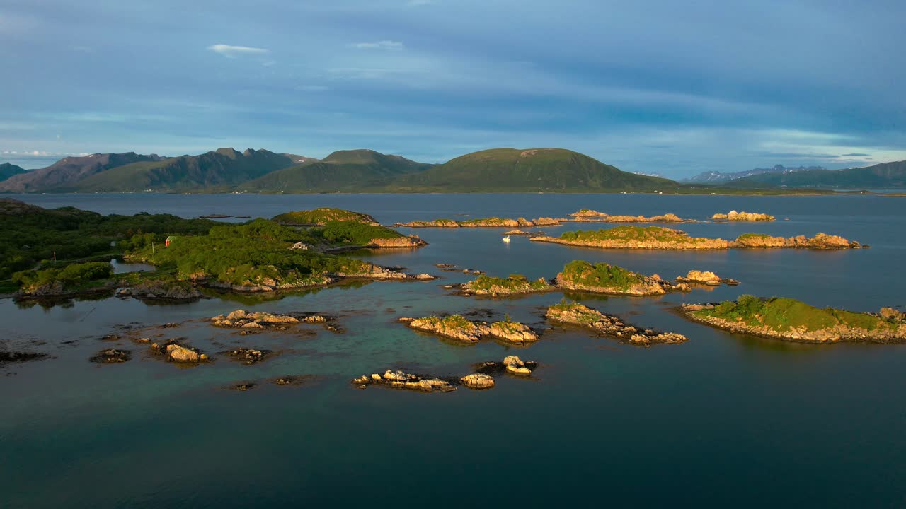 Low forward aerial view of small rocky islands along the Northern Norway coastline in the summer under a midnight sun