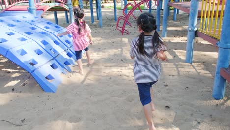 active little sisters are running in the outdoor playground in the park. happy child girls smiling and laughing on children playground. the concept of play is learning in childhood.