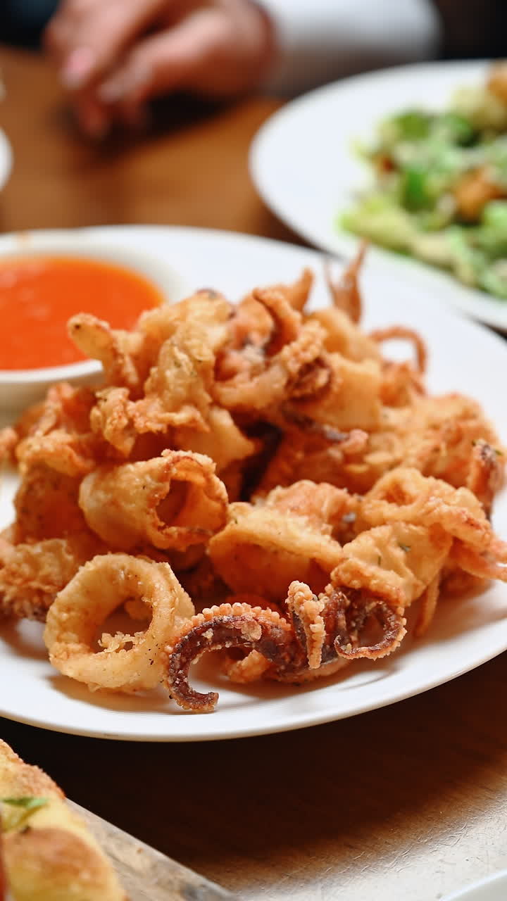 Piatto di frutti di mare fritti servito con salsa su un piatto durante un pasto. I frutti di mare fritti vengono serviti su un piatto con una piccola ciotola di salsa accanto durante un pasto al ristorante.