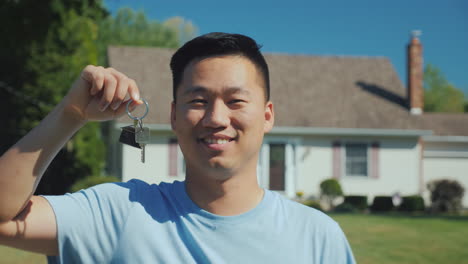 portrait of a young asian man with a house key in his hand looking at the camera against the backgro