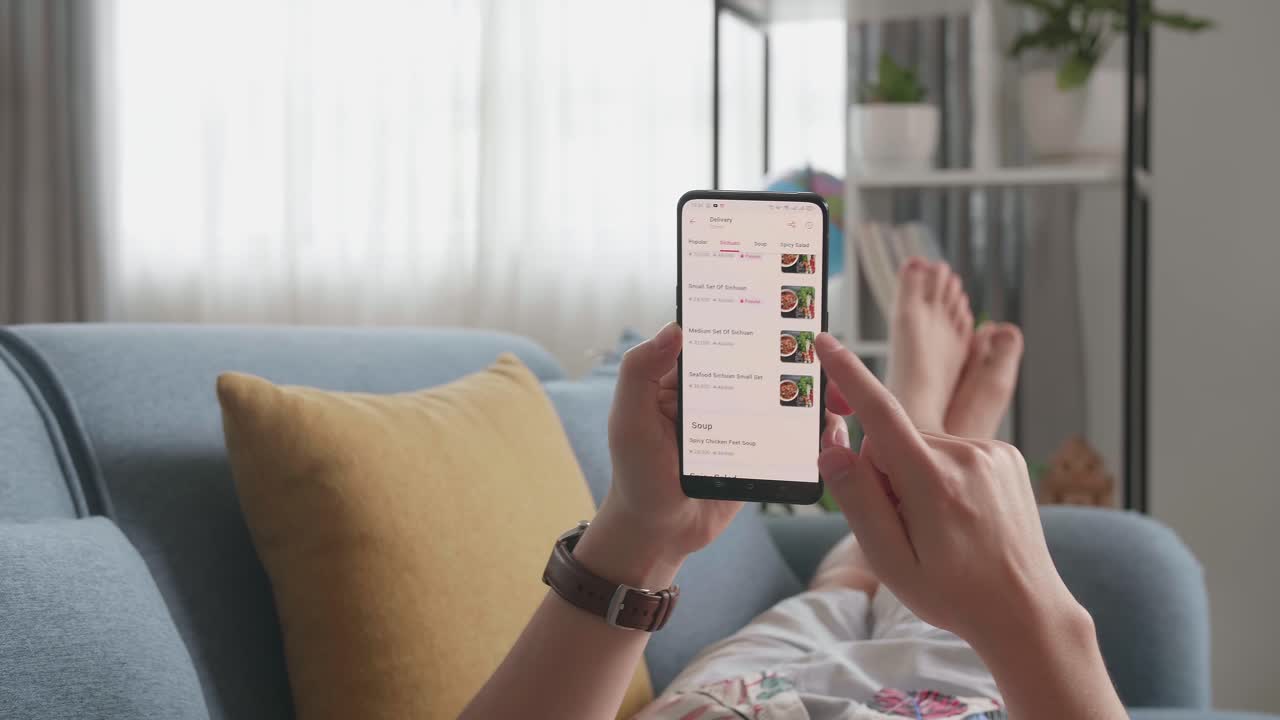 Close Up Of Hand Man At Home Lying On Couch In Living Room Using Smartphone Buys In Internet Shop. Man Orders Food In An Online Store Using A Smartphone