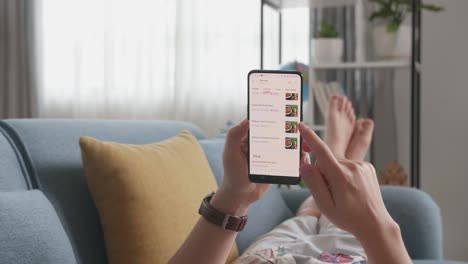 close up of hand man at home lying on couch in living room using smartphone buys in internet shop. man orders food in an online store using a smartphone
