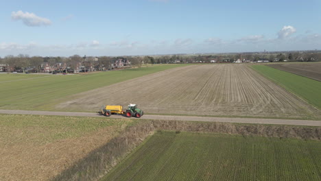 aerial of tractor with large tank driving between green meadows at the edge of rural town