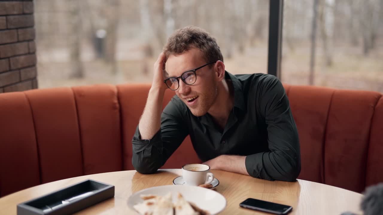 Giovane uomo pensieroso seduto in un caffè ha un'idea interessante e sorride.