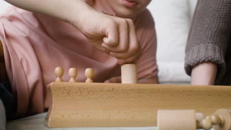 close-up view of a boy with down syndrome and his mother playing with wooden toy sitting on the bed in the bedroom at home