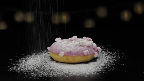 tasty fresh donut lay on black surface and gets sprinkle with icing sugar powder