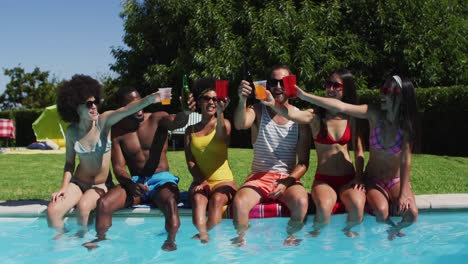 group of diverse friends toasting drinks while sitting by the pool