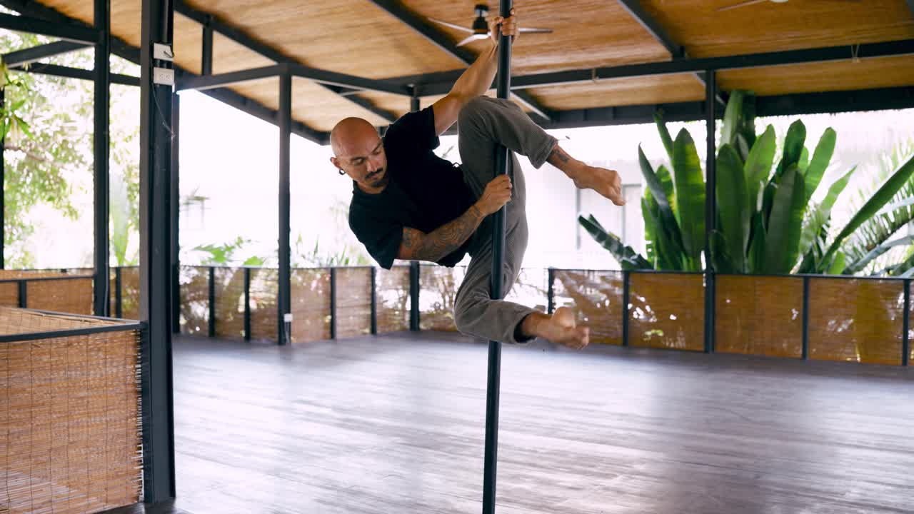 Uomo che pratica pole fitness acrobatico in uno studio tropicale