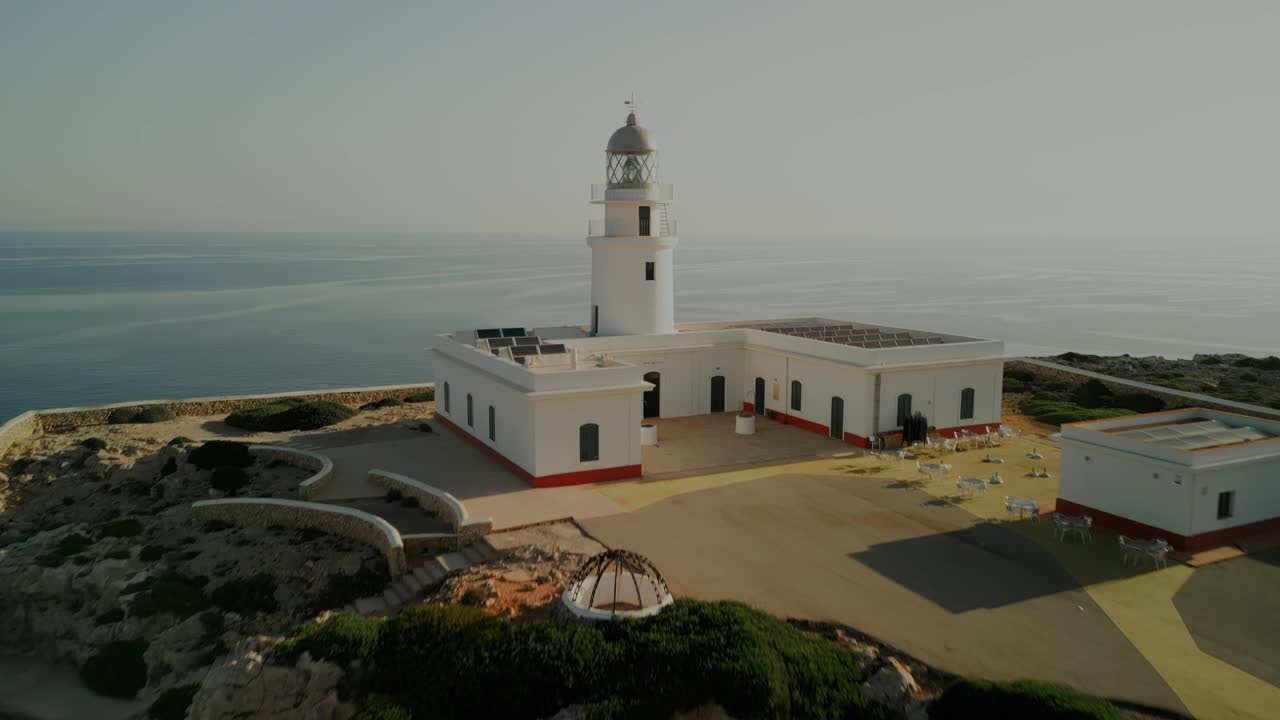 Drone dolly approach to lighthouse over inland hills along Menorca coast with scattered trees and rural scenery