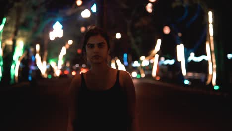 brunette woman in a black dress looking at the camera in a street scene full of cars and colored lights