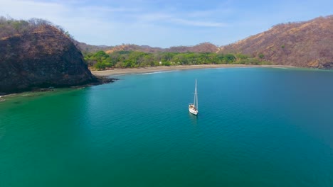 aerial shot flying past an anchored sailing yacht in an empty calm water bay off the coast of one of the most beautiful white sand beaches in the world