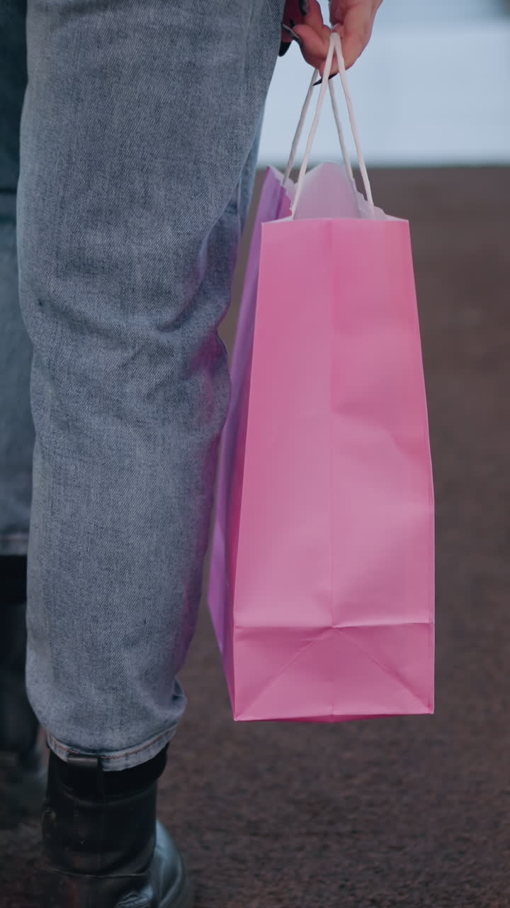 푸른 청바지와 검은 부츠를 입은 여성이 아래로 내려가는 에스컬레이터를 고, 두 개의 쇼핑 가방을 들고, 현대 쇼핑몰 설정에서 흐릿한 배경