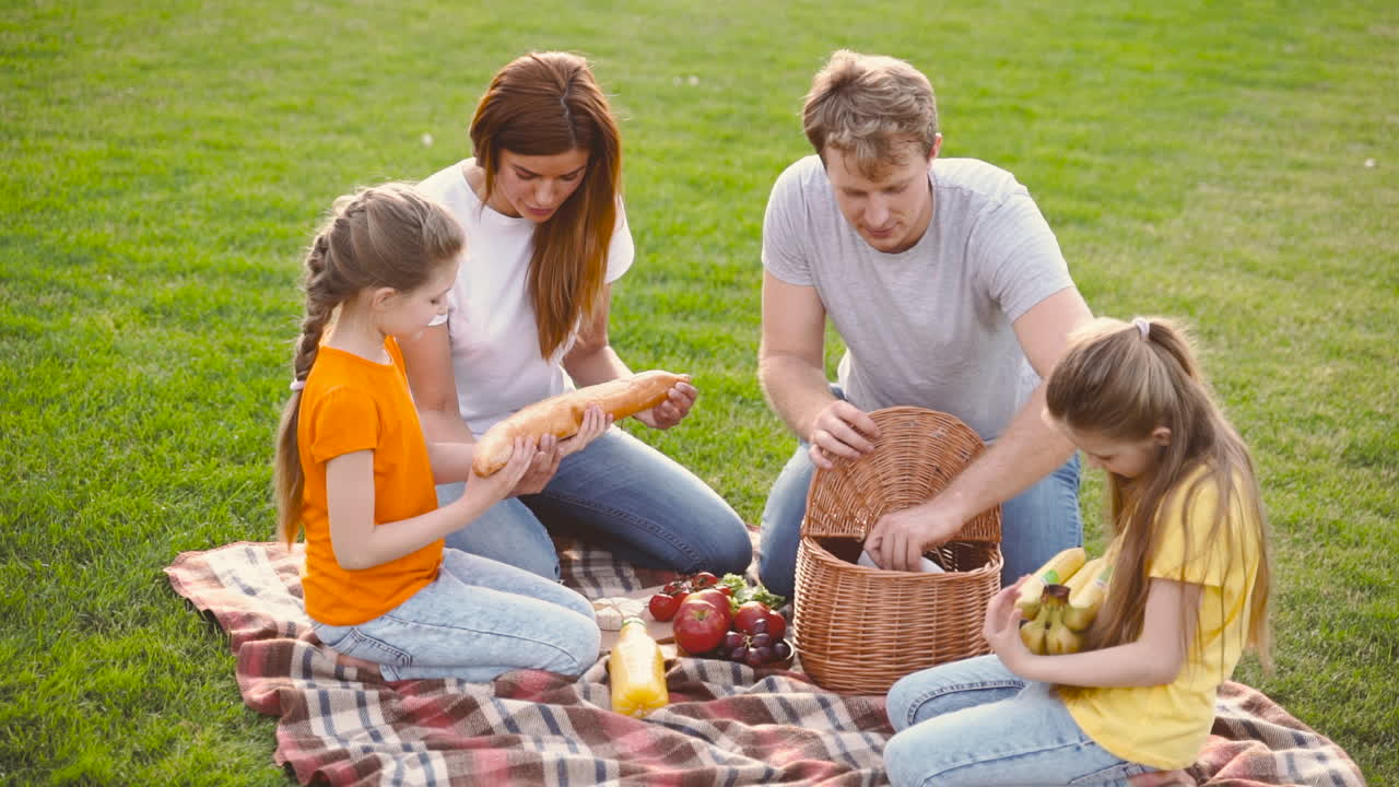 padres felices con dos hijas pequeñas haciendo un picnic juntos en un prado verde en el parque