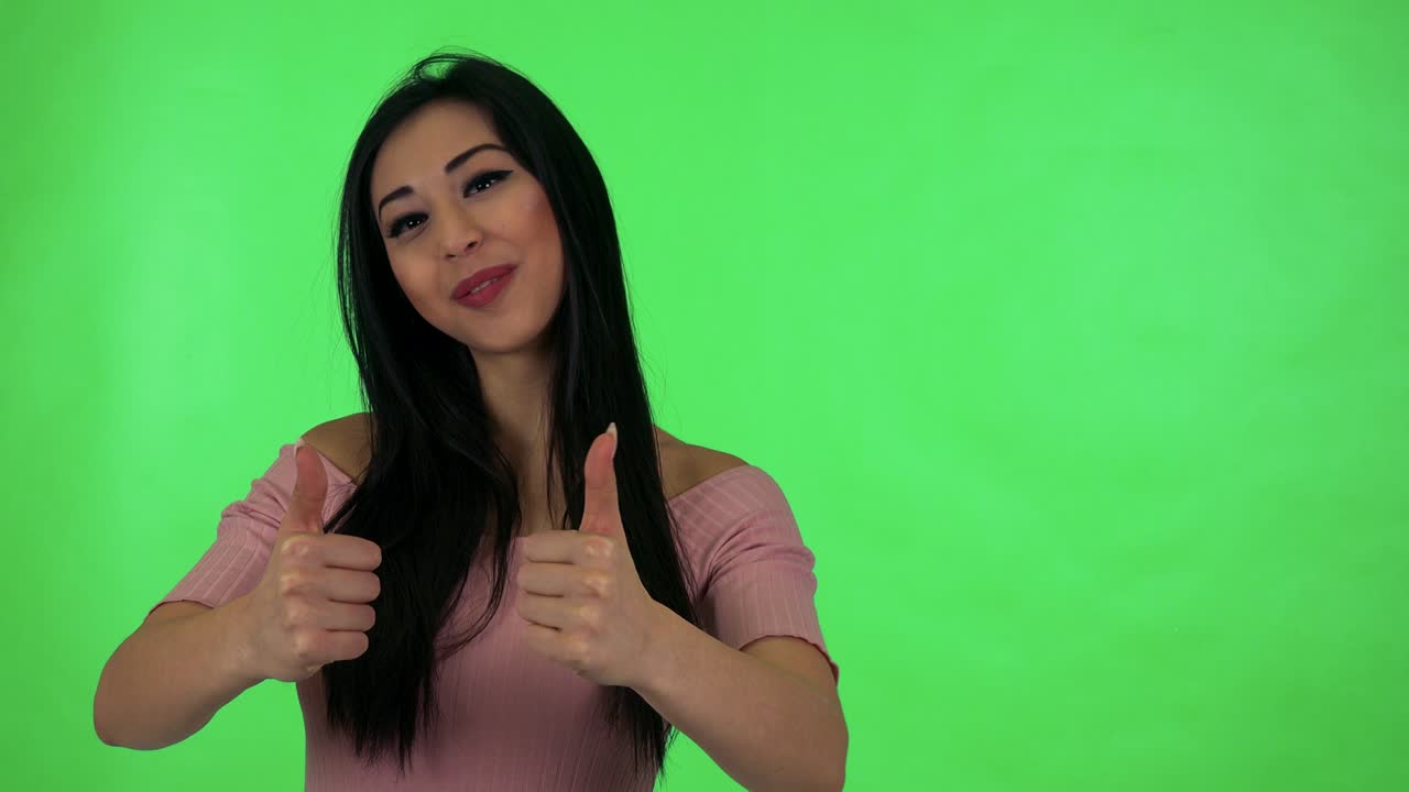 una joven atractiva asiática muestra los pulgares en el acuerdo - estudio de pantalla verde