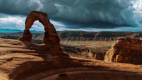 scenic and cinematic dark thunderstorm clouds time-lapse at the famous delicate arch rock among the arches national park hiking landmarks in utah, arizona, america usa. cinemagraph seamless video.