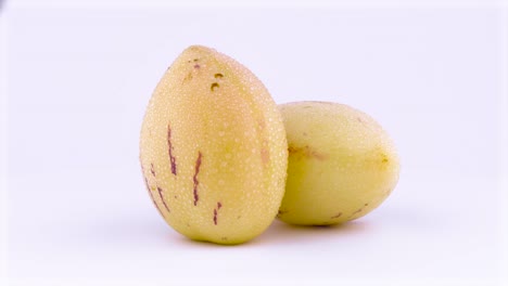 two whole mature yellow pepino fruits with water drops. rotating on the turntable. isolated on the white background. close-up. macro.