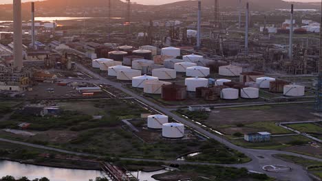 drone establish of large vat tanks at oil refinery surrounded by piping and flare stacks