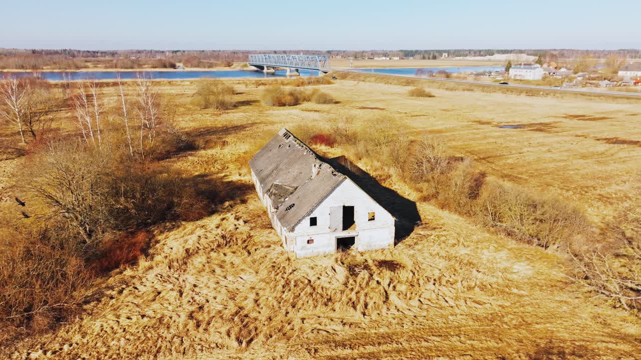 Latvian spring field, derelict building, distant bridge, and gliding black birds