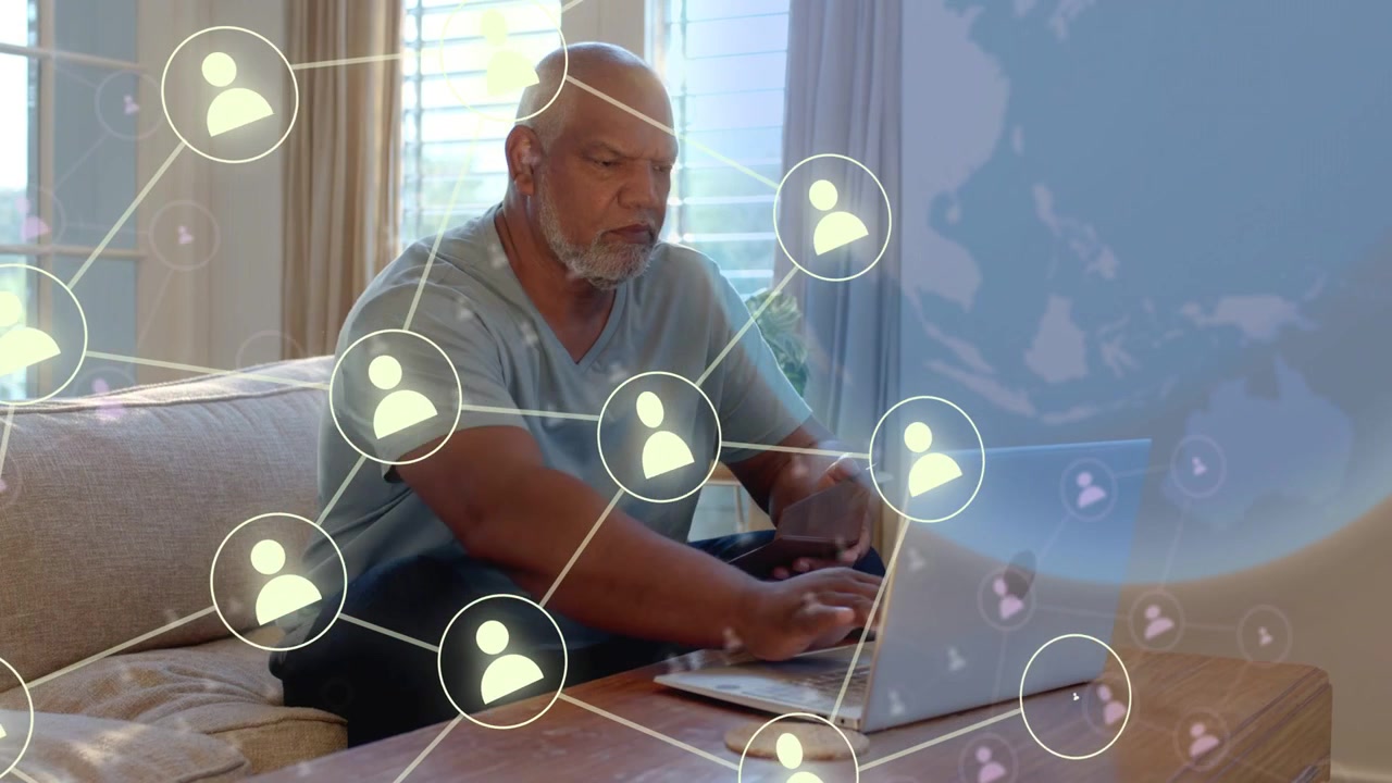 En senior skriver på en bærbar computer og trykker på telefonen derhjemme, hvilket skaber et udvidende netværk for teknologiforbindelse.