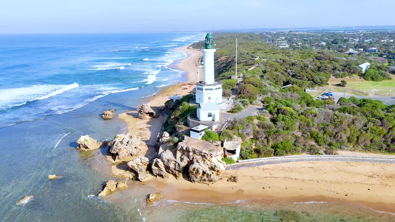 Aerial footage captures the Point Lonsdale Lighthouse, rocky coastline, and ocean waves under bright daylight in Victoria, Australia