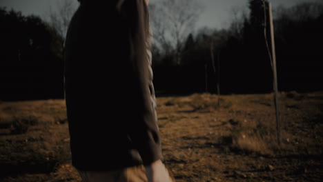 follow shot of a young caucasian male photographer out in nature, holding a dslr mirrorless camera and walking toward a forest at sunrise or sunset