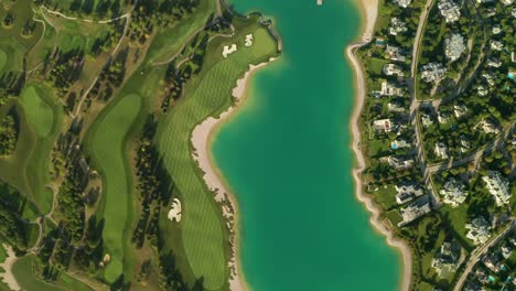 aerial overhead view of a turquoise lake next to a golf resort with beautiful abstract patterns, sand traps, trees tennis courts, and a