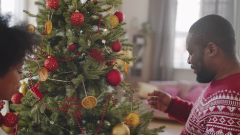 una pareja afroamericana decorando el árbol de navidad en casa
