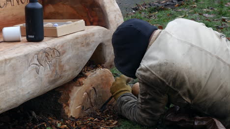 a man calving a wooden bench with a chisel in a park