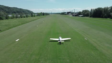 Pequeño-Avión-Seguido-Por-Un-Dron-Mientras-Despegaba-En-Un-Pequeño-Aeropuerto-Desde-Una-Franja-De-Césped