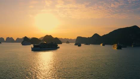 many cruise ships anchored at halong bay back lit with rising sun, vietnam