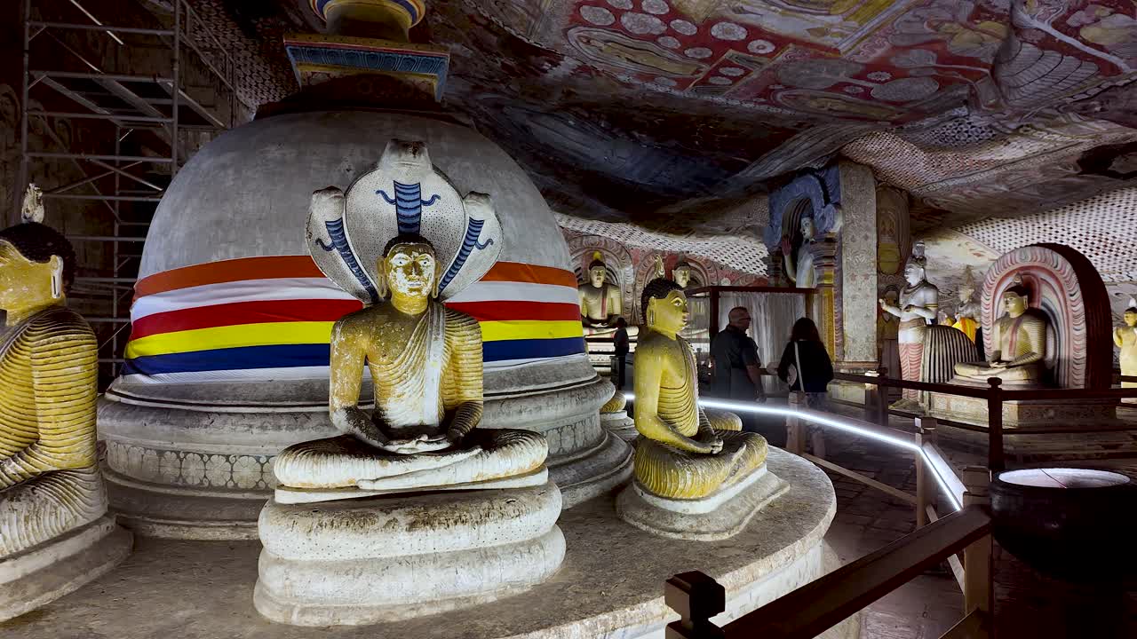 Seated Buddhas around a stupa inside the historic Dambulla Cave Temple in Sri Lanka, showcasing intricate artistry and spiritual ambiance. Pan Right Shot