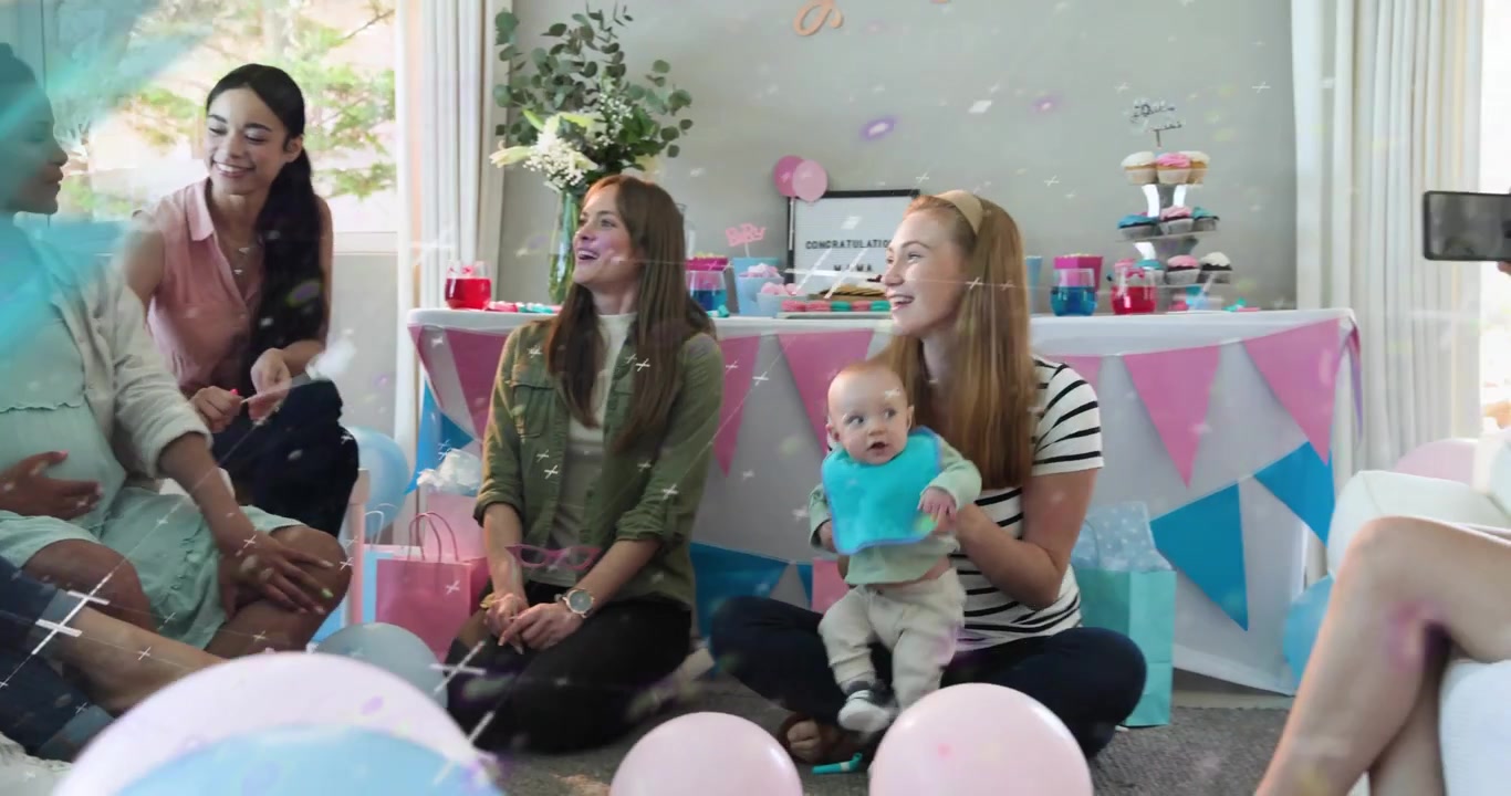 Amigos chocando palitos y lanzando confeti alrededor de mujer embarazada en baby shower mientras el teléfono hace un paneo