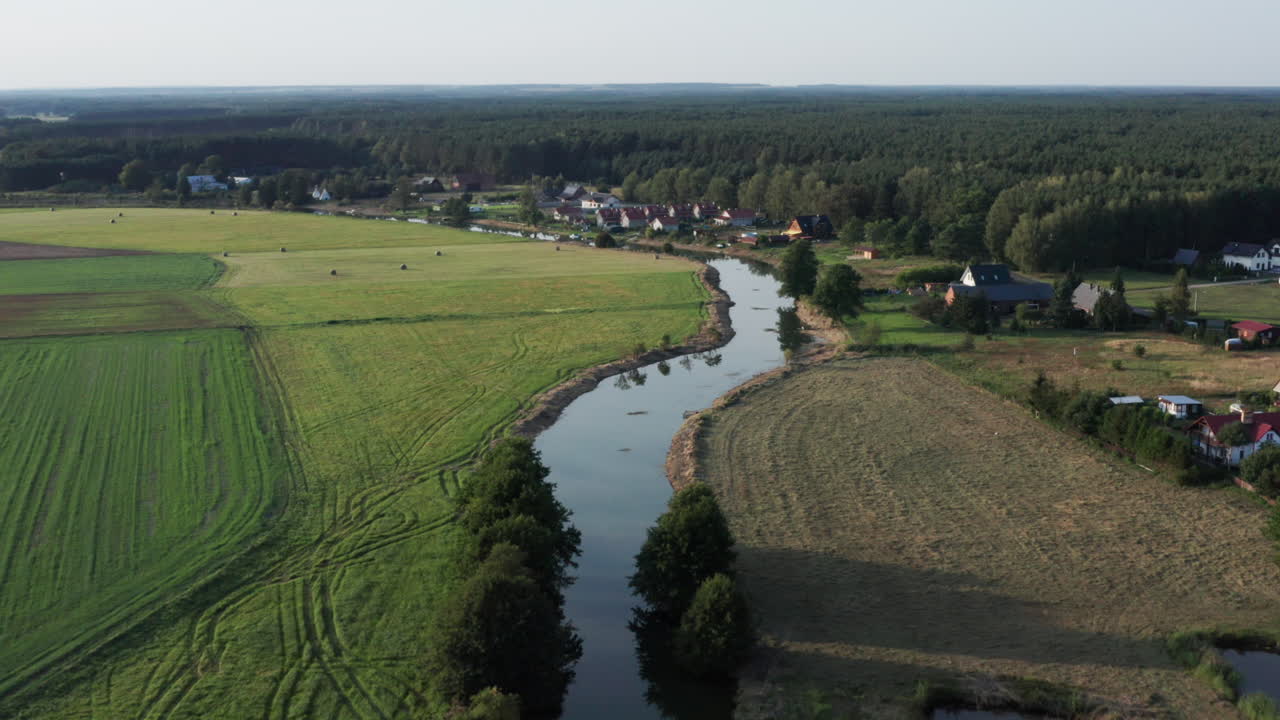 숲 옆 작은 마을의 들판과 농장 사이에 있는 굽이치는 강의 공중 시골 사진