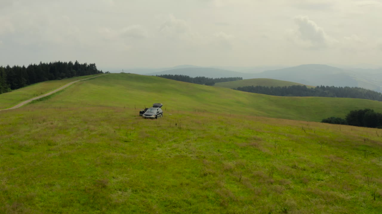 Aerial shot of car parked on scenic mountain meadow with rolling hills in background. Bieszczady, Poland