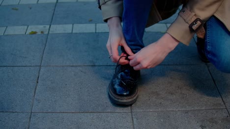 una mujer apretando el encaje de sus zapatos casuales en la calle, apresurándose en el trabajo, un primer plano del movimiento de atar el zapato.