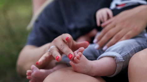 unrecognized caucasian woman holding her baby in hands. mom's hand strokes her child's tiny bare feet. close up. blurred backdrop.
