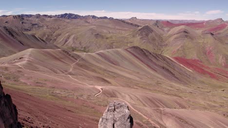 rugged rock formations rise over a colorful mountain range in peru, under a clear sky.