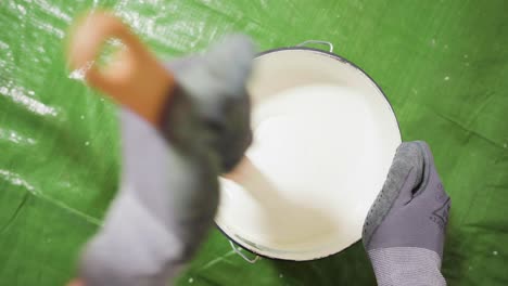 man mixing white paint in a bucket with a wooden stick
