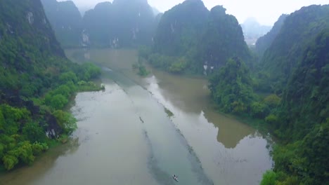 cinematic drone footage of majestic limestone peaks in misty and foggy weather. ricefields in wild jungle in the spring with boat tour canal in tam coc, ninh binh, vietnam