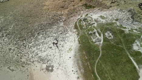 downward arc aerial view of a ruined building next to sandy beach and ocean