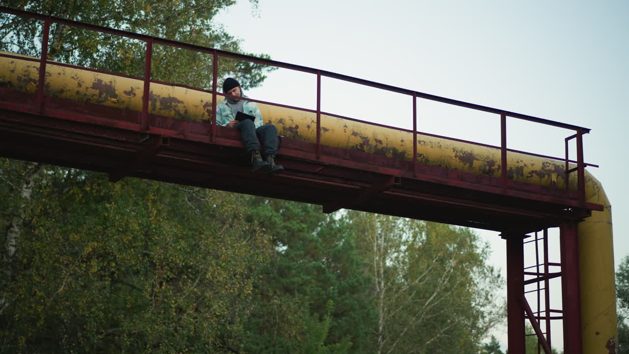 white hiker perched on rusted pipeline, adventurer scanning forest canopy, boots dangling over metal railing, panoramic vista, raw industrial texture, courageous mood, travel and exploration vibe