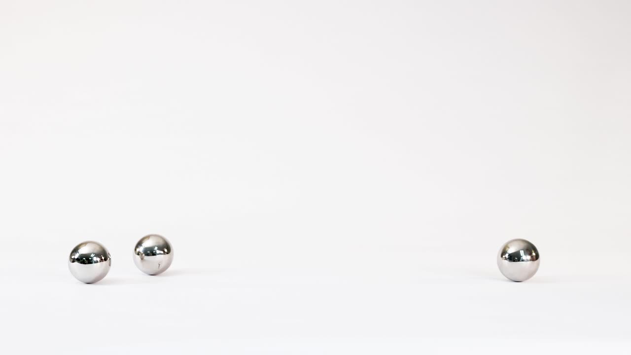 Shiny chrome spheres roll smoothly across a bright white background under soft studio lighting